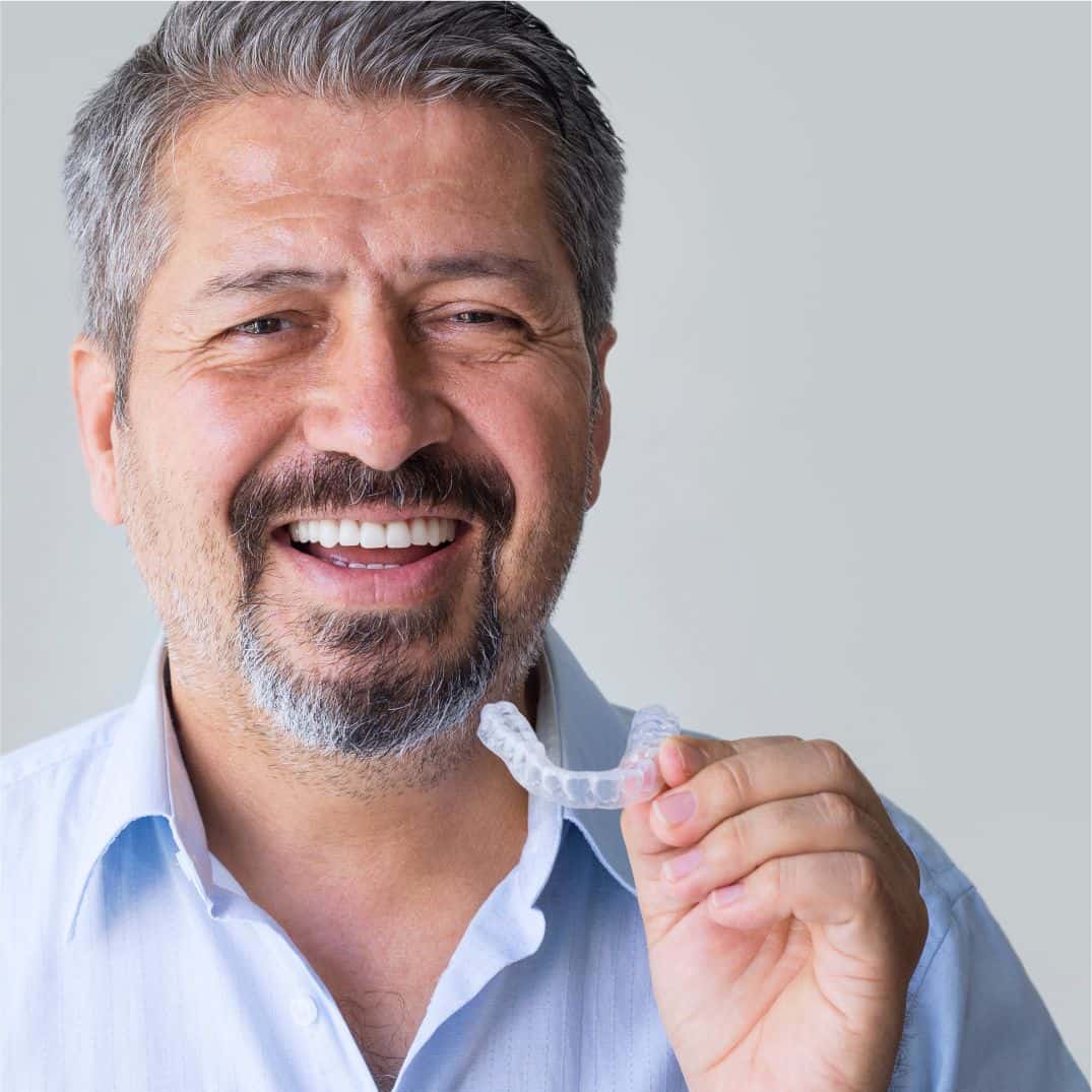 A woman smiling while holding a small, discreet oral appliance for sleep apnea.